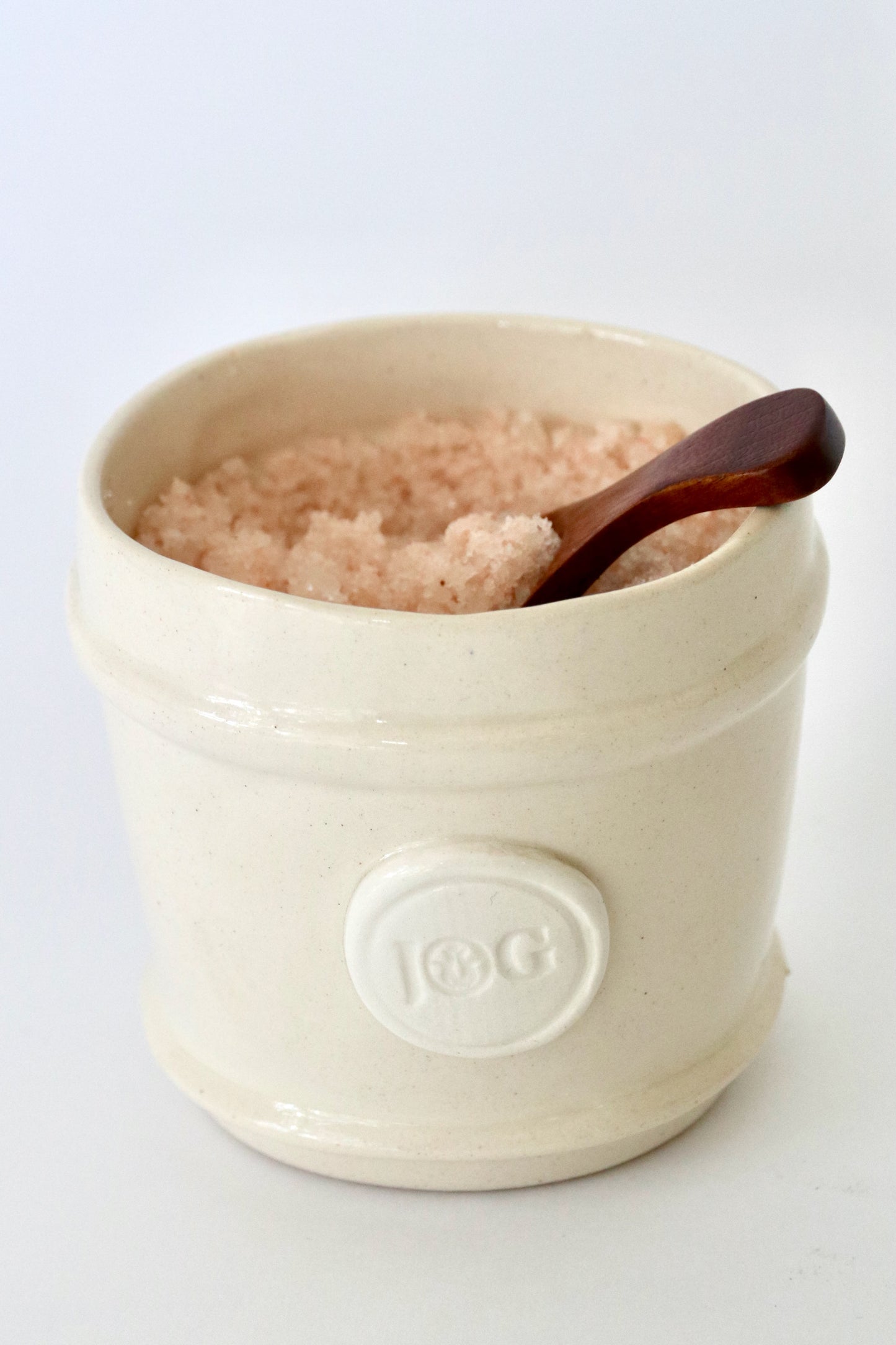 White ceramic container with pink salt and a wooden spoon on a white background