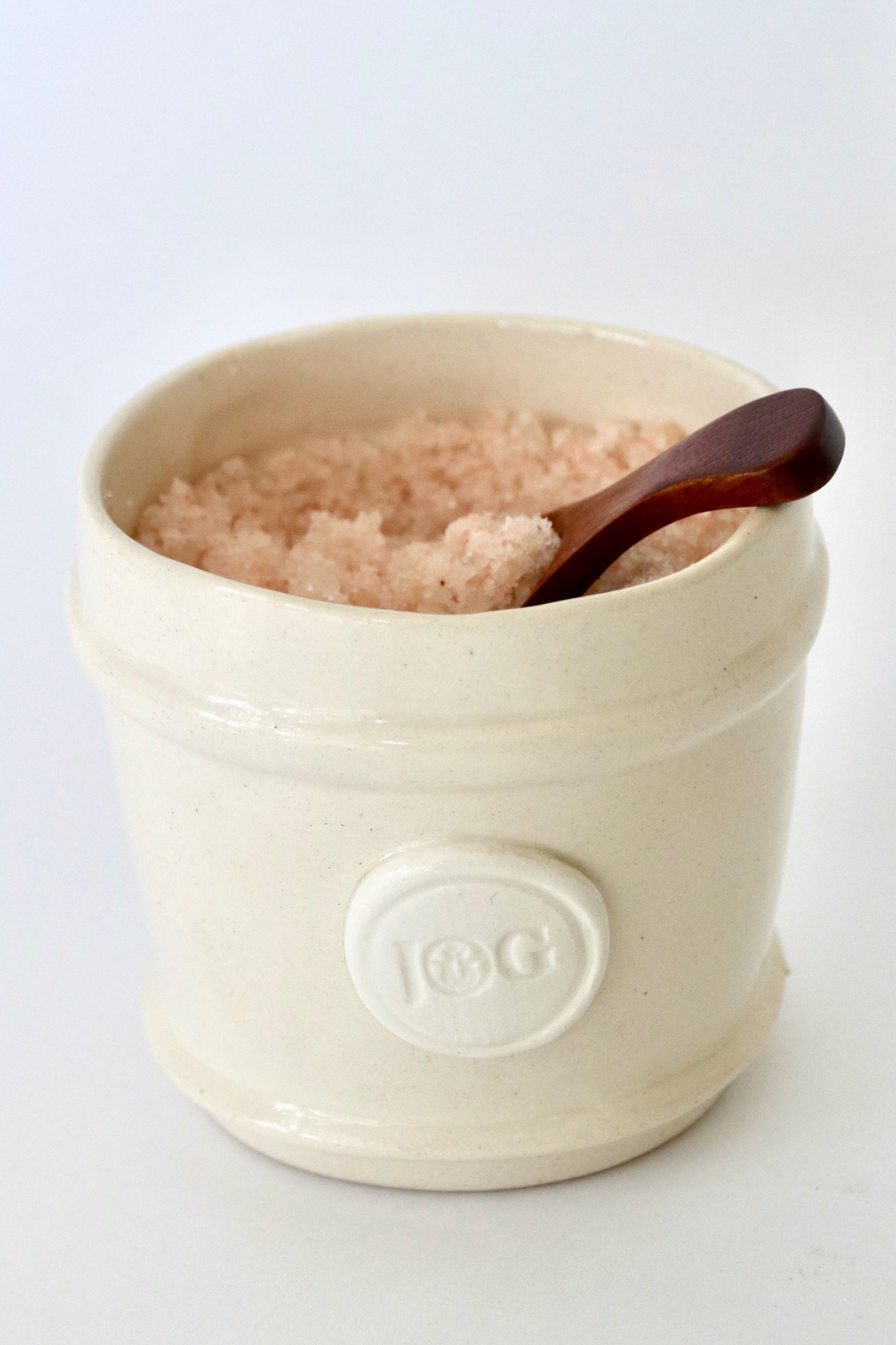 White ceramic container with pink salt and a wooden spoon on a white background